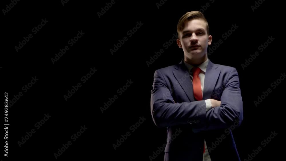 a young man of Caucasian appearance in a business suit quickly and very confidently emerging from the shadows into the light and crossing his arms on his chest a young man of Caucasian appearance in a business suit quickly and very confidently emerging from the shadows into the light and crossing his arms on his chest