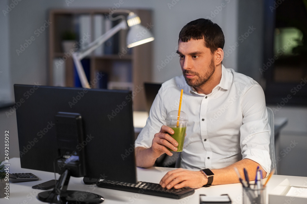 business, overwork, deadline and people concept - businessman with computer working and drinking green smoothie at night office business, overwork, deadline and people concept - businessman with computer working and drinking green smoothie at night office