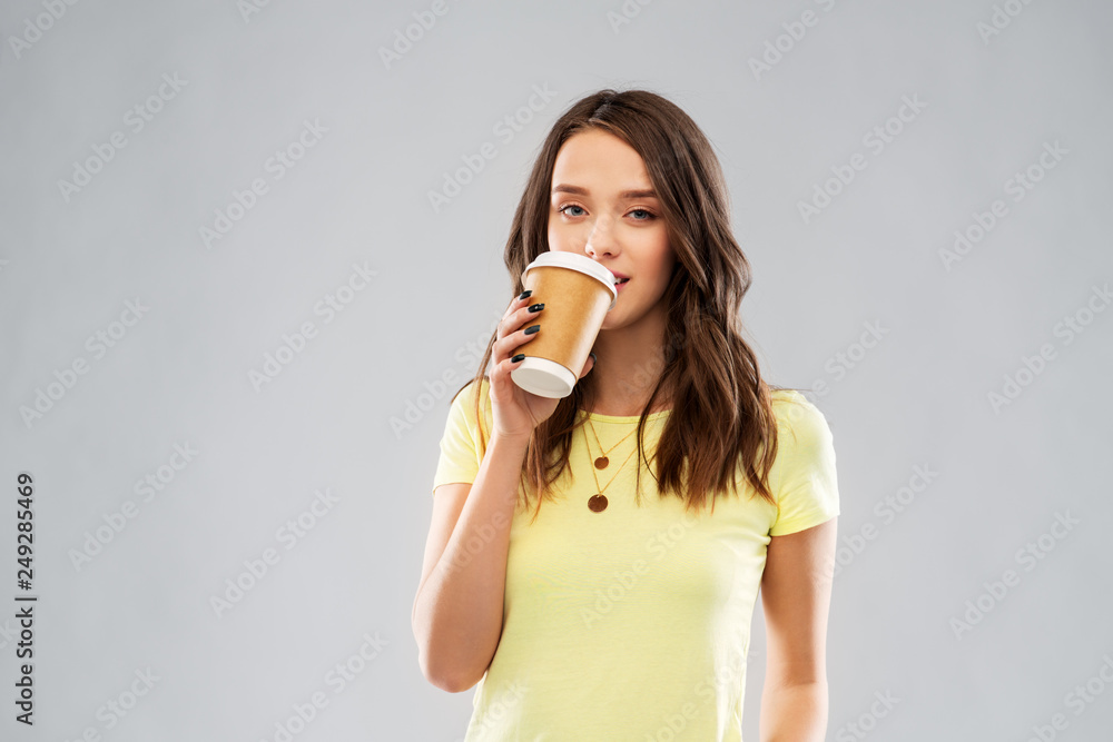 takeaway and people concept - young woman or teenage girl in yellow t-shirt drinking coffee over grey background takeaway and people concept - young woman or teenage girl in yellow t-shirt drinking coffee over grey background