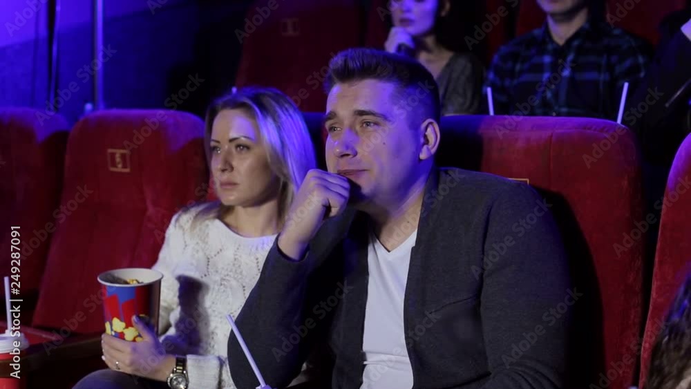 Close-up portrait of a couple in love in the cinema, they watch a very sad movie and cry. Couple on a date at the cinema. Young people watch a chick flick in the cinema. Close-up portrait of a couple in love in the cinema, they watch a very sad movie and cry. Couple on a date at the cinema. Young people watch a chick flick in the cinema.