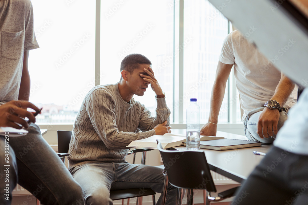 Worried man with head in hands surrounded by friends sitting on desk Worried man with head in hands surrounded by friends sitting on desk