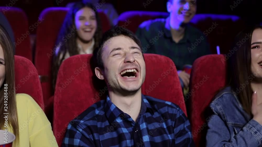 Close-up portrait of a young laughing man in a movie theater. A group of friends watching a funny movie in the cinema, they together laugh hard at the joke. Close-up portrait of a young laughing man in a movie theater. A group of friends watching a funny movie in the cinema, they together laugh hard at the joke.
