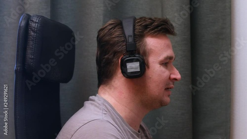 A young man sitting in a chair listening to music in headphones incredibly feeling the rhythm of music. Musical inspiration at work