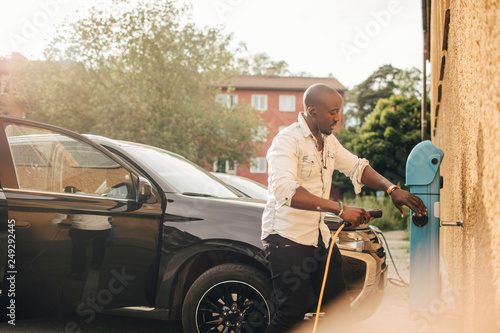 Man connecting electric cable for car in charging station at house photo