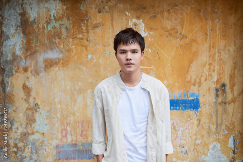 Asian man in casual clothes standing on old wall background.