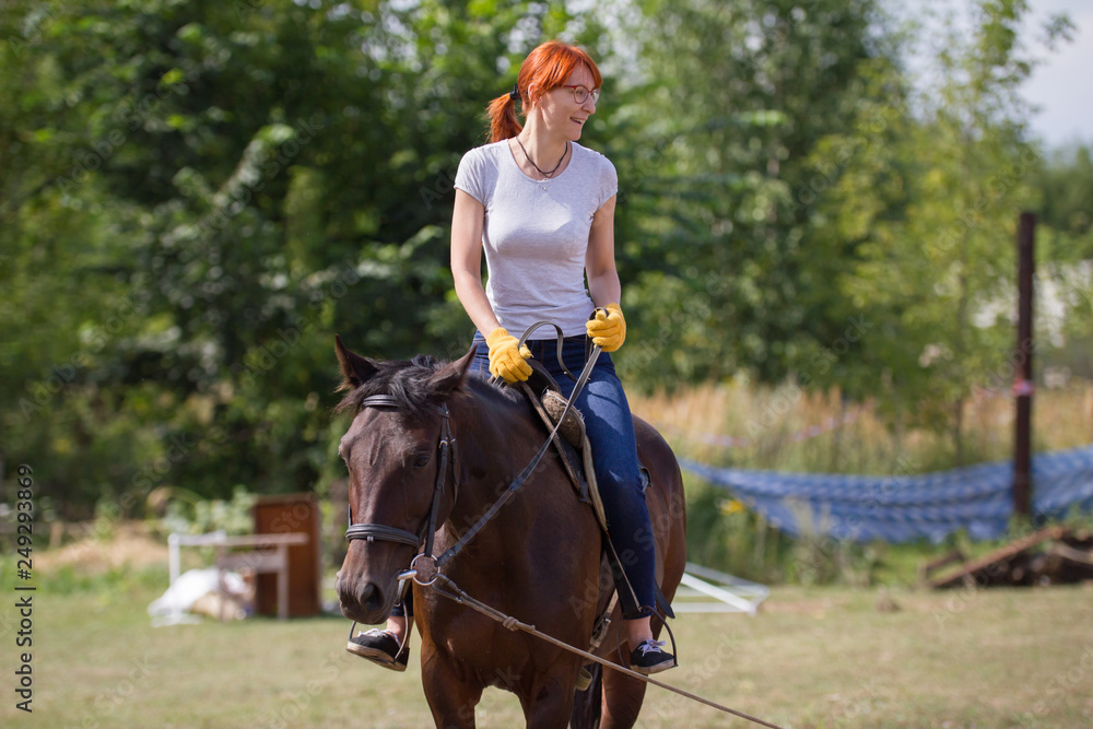 A redhead smiling woman riding a horse on the field. A redhead smiling woman riding a horse on the field.