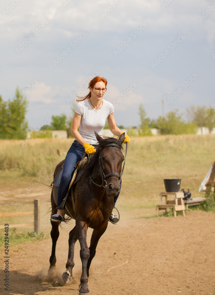 A redhead woman in yellow gloves riding a horse on the field.