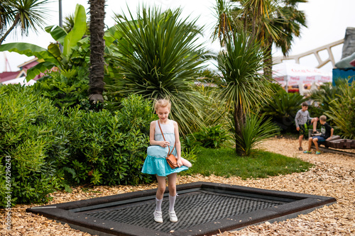 Blonde girl in white and blue dress playing in the playground in the summer park of entertainments