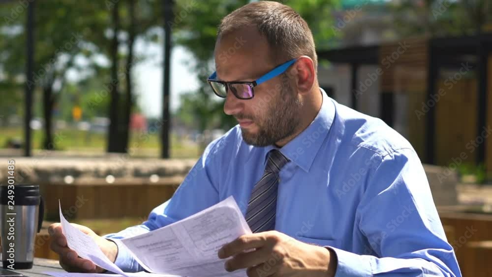 Young businessman reading documents by table in city park Young businessman reading documents by table in city park