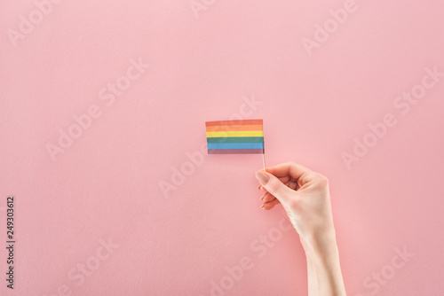 partial view of female hand with paper rainbow flag on pink background, lgbt concept