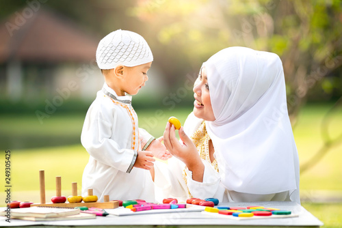 uslim mother teaching her little son to play math computation beads in the garden on grass field near beautiful lake. Muslim family concept.