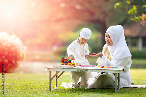 uslim mother teaching her little son to play math computation beads in the garden on grass field near beautiful lake. Muslim family concept.