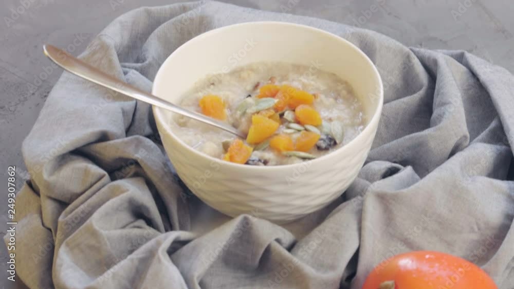 Healthy food. Oatmeal in a deep bowl with persimmon, dried apricots, prunes, walnuts, pumpkin seeds and sesame. Slow panning Healthy food. Oatmeal in a deep bowl with persimmon, dried apricots, prunes, walnuts, pumpkin seeds and sesame. Slow panning