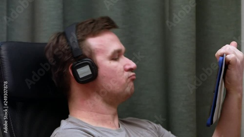 man sitting in a chair listening to heavy music in headphones from the tablet .