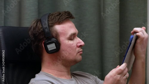 man sitting in a chair listening to heavy music in headphones from the tablet .
