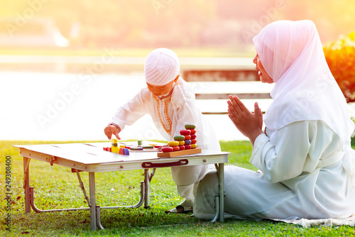 uslim mother teaching her little son to play math computation beads in the garden on grass field near beautiful lake. Muslim family concept. photo