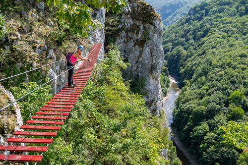 Female tourist on a via ferrata bridge in Vadu Crisului, Padurea Craiului mountains, Romania, with the Crisul Repede defile/gorge meandering below. photo