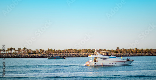 Yacht and a dark grey boat at in the blue sea background of a sea horizon goes towards sunset from United Arab Emirates, Oil Painting Background concept. 