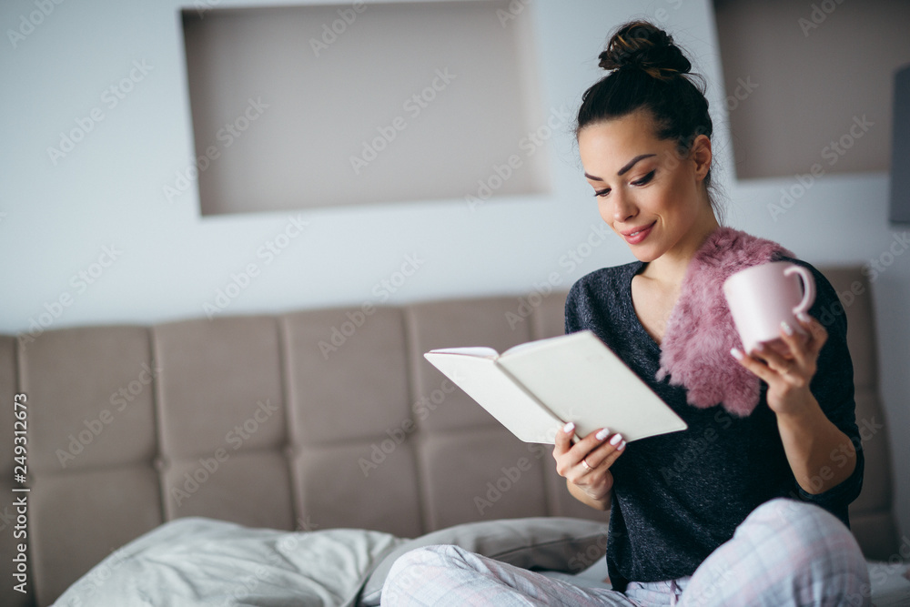 Young woman relaxing on her bed at home and reading book. Lifestyle concept