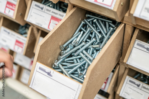 persons hand choose suitable bolt or screw from the crate in hardware store b