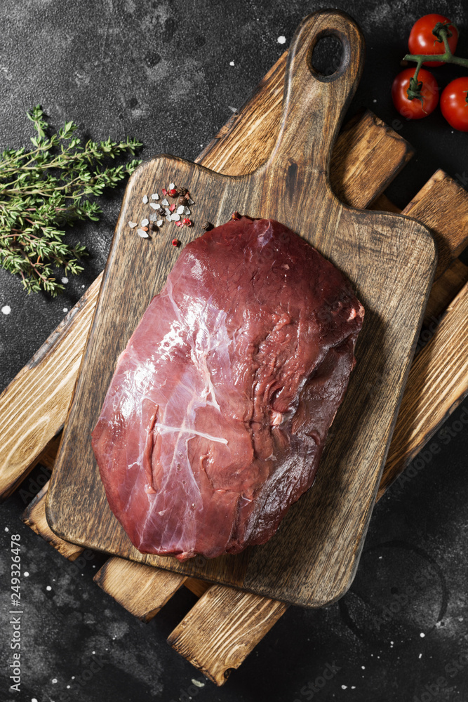 Raw reindeer meat on wooden Board on dark background