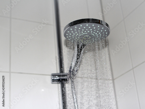 Flowing water from modern shower head at tiled bathroom interior, nobody