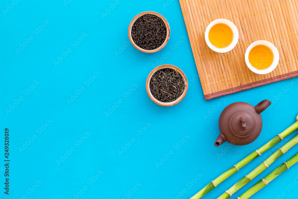 Chinese tea ceremony concept. Tea pot, tea cup, dry tea leaves, bamboo mat on blue background top view copy space pattern Chinese tea ceremony concept. Tea pot, tea cup, dry tea leaves, bamboo mat on blue background top view copy space pattern