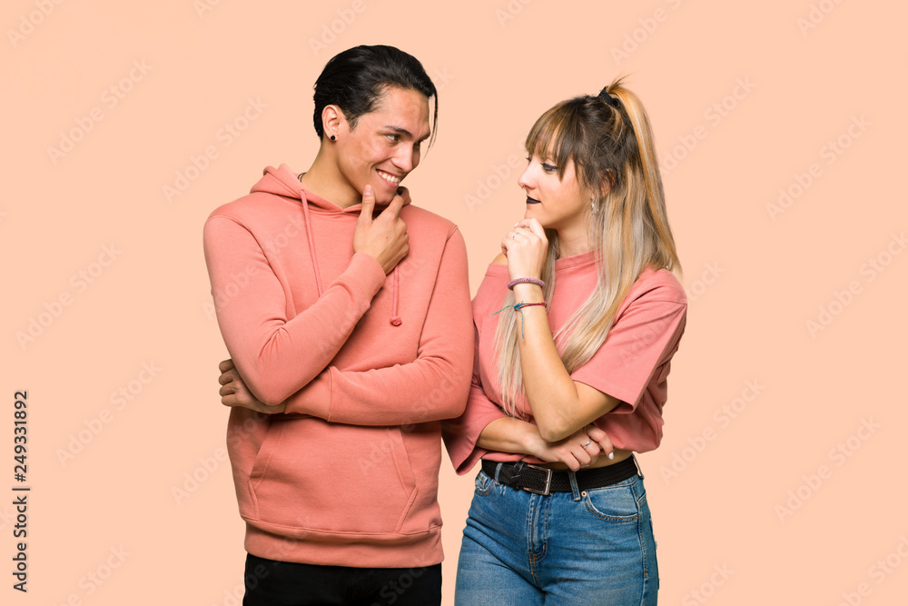 Young couple looking to the side with the hand on the chin over pink background Young couple looking to the side with the hand on the chin over pink background