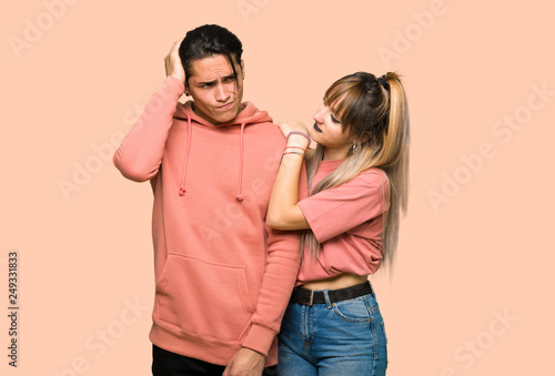 Young couple having doubts while scratching head over pink background