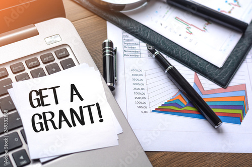 Desk with business accessories, calculator, documents with charts, fountain pen, laptop and paper for notes with text Get a grant. With lights effects