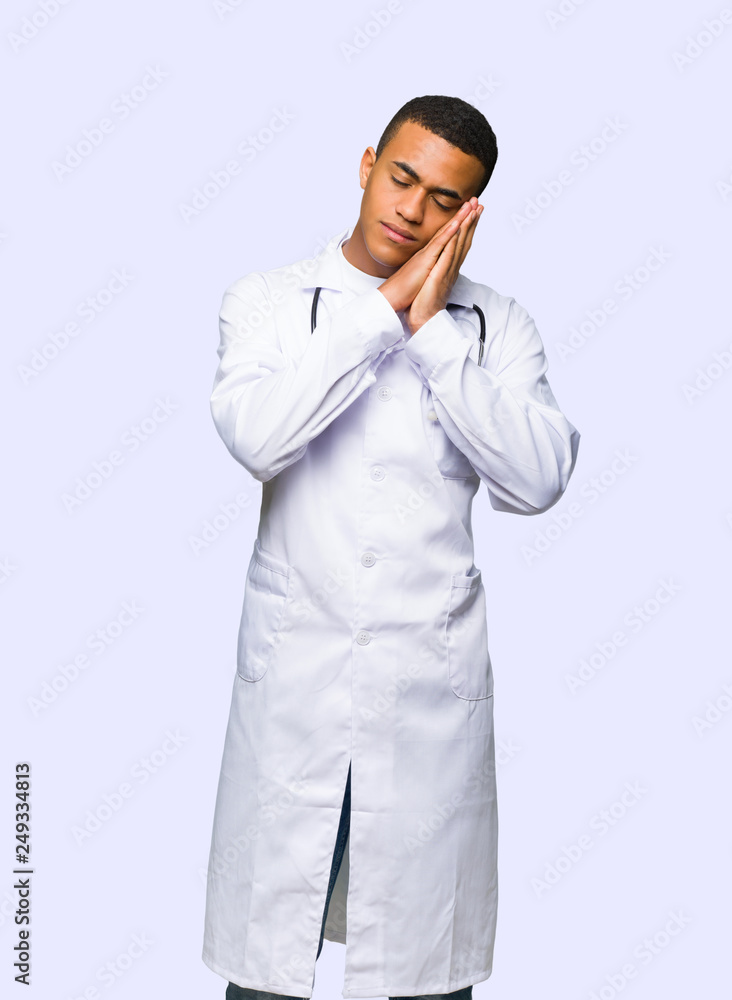Young afro american man doctor making sleep gesture in dorable expression on isolated background Young afro american man doctor making sleep gesture in dorable expression on isolated background