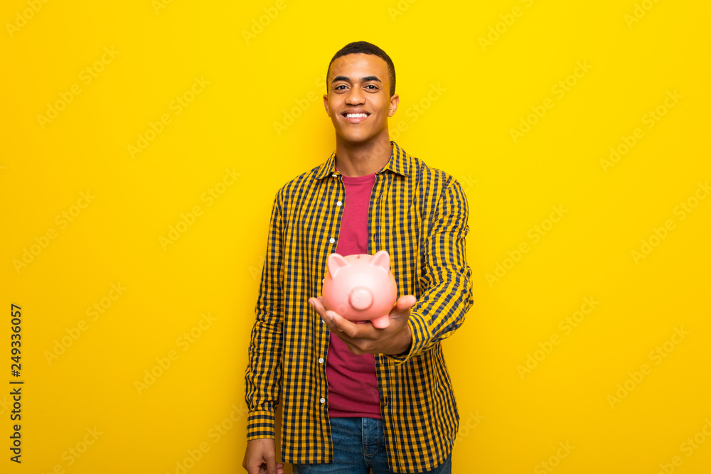 Young afro american man on yellow background holding a piggybank Young afro american man on yellow background holding a piggybank