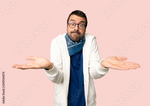 Handsome man with glasses having doubts while raising hands and shoulders on isolated pink background