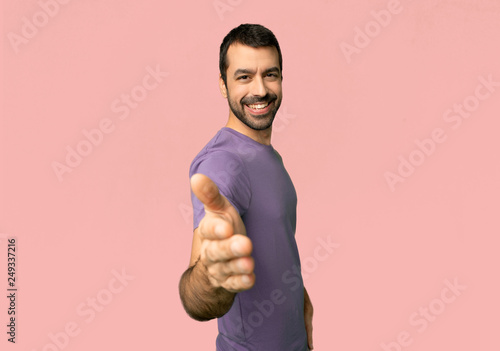 Handsome man shaking hands for closing a good deal on isolated pink background
