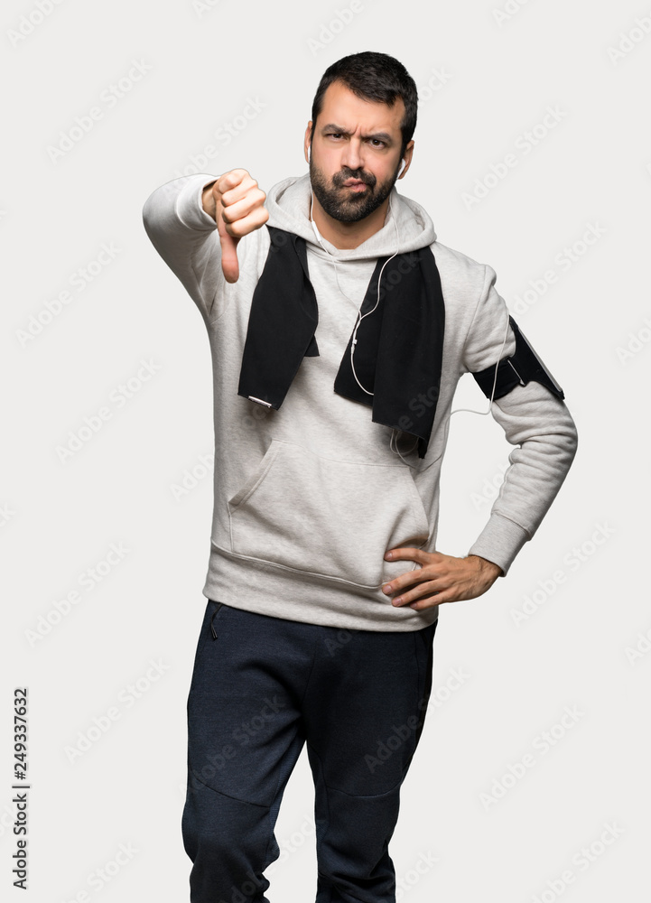 Sport man showing thumb down sign with negative expression over isolated grey background Sport man showing thumb down sign with negative expression over isolated grey background
