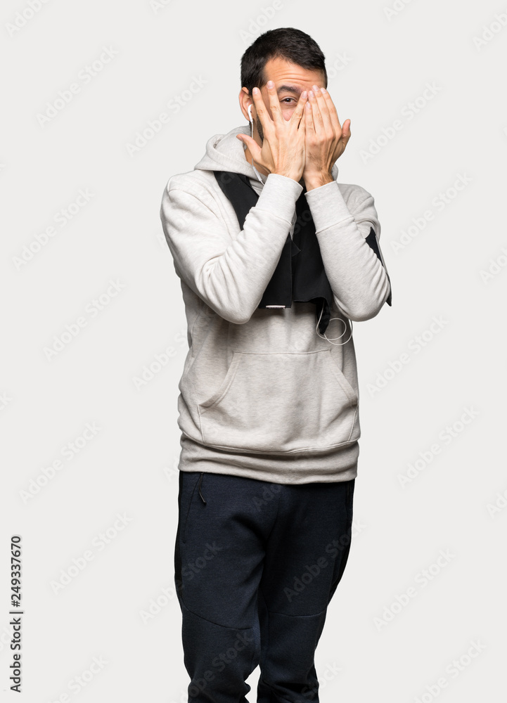 Sport man covering eyes by hands and looking through the fingers over isolated grey background