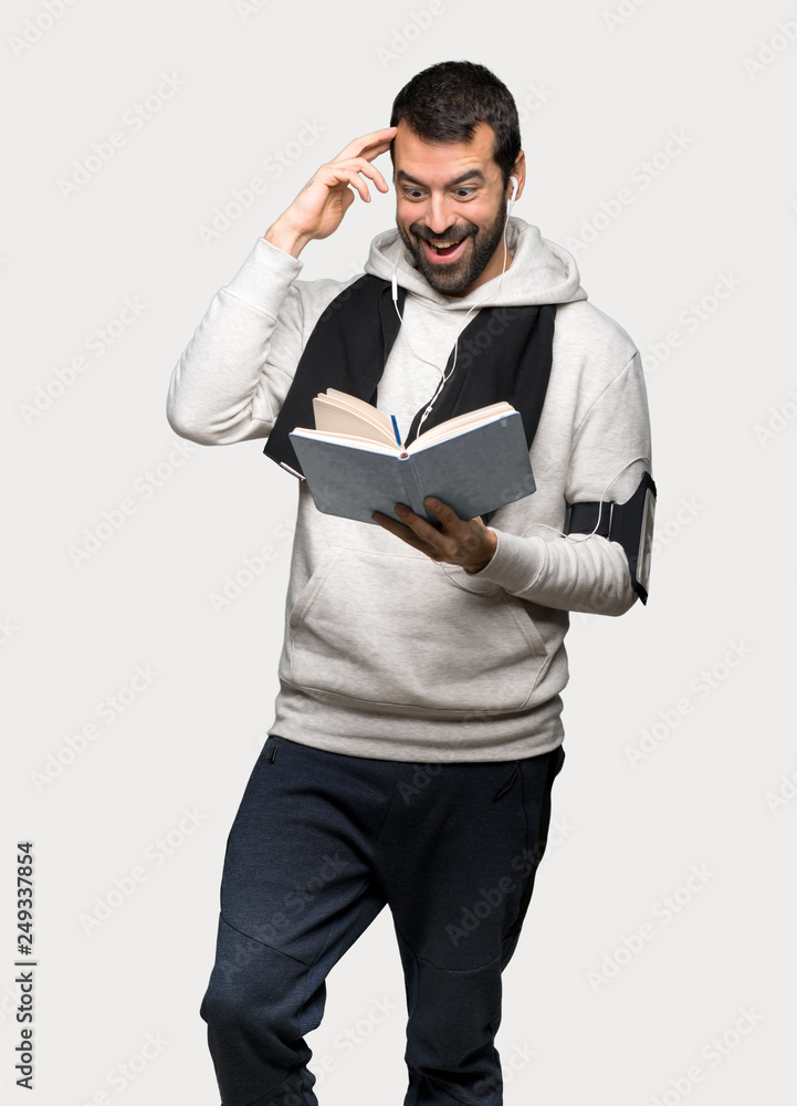 Sport man surprised while enjoying reading a book over isolated grey background Sport man surprised while enjoying reading a book over isolated grey background