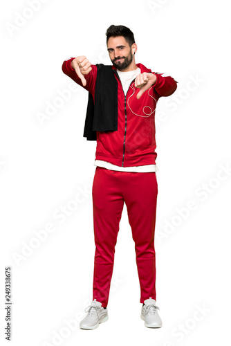Full-length shot of Handsome sportman showing thumb down with both hands on isolated white background
