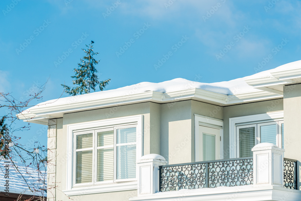 A typical american house in winter. Fragment of a house with roof and window covered by snow. Daylight and blue sky.