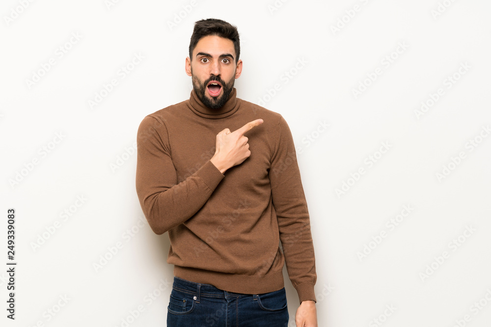 Handsome man over white wall pointing to the side to present a product Handsome man over white wall pointing to the side to present a product