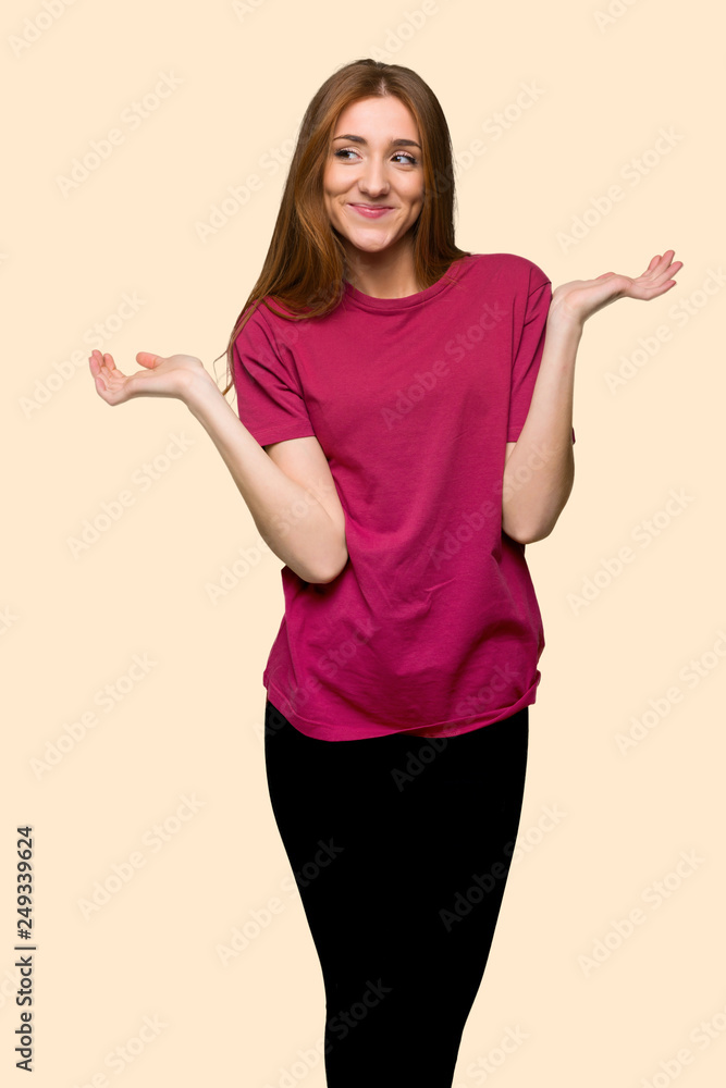 Young redhead girl having doubts while raising hands and shoulders on isolated yellow background Young redhead girl having doubts while raising hands and shoulders on isolated yellow background