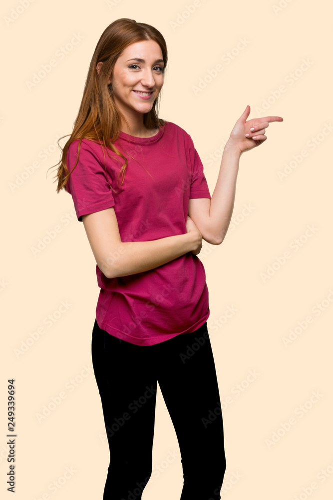 Young redhead girl pointing finger to the side in lateral position on isolated yellow background Young redhead girl pointing finger to the side in lateral position on isolated yellow background
