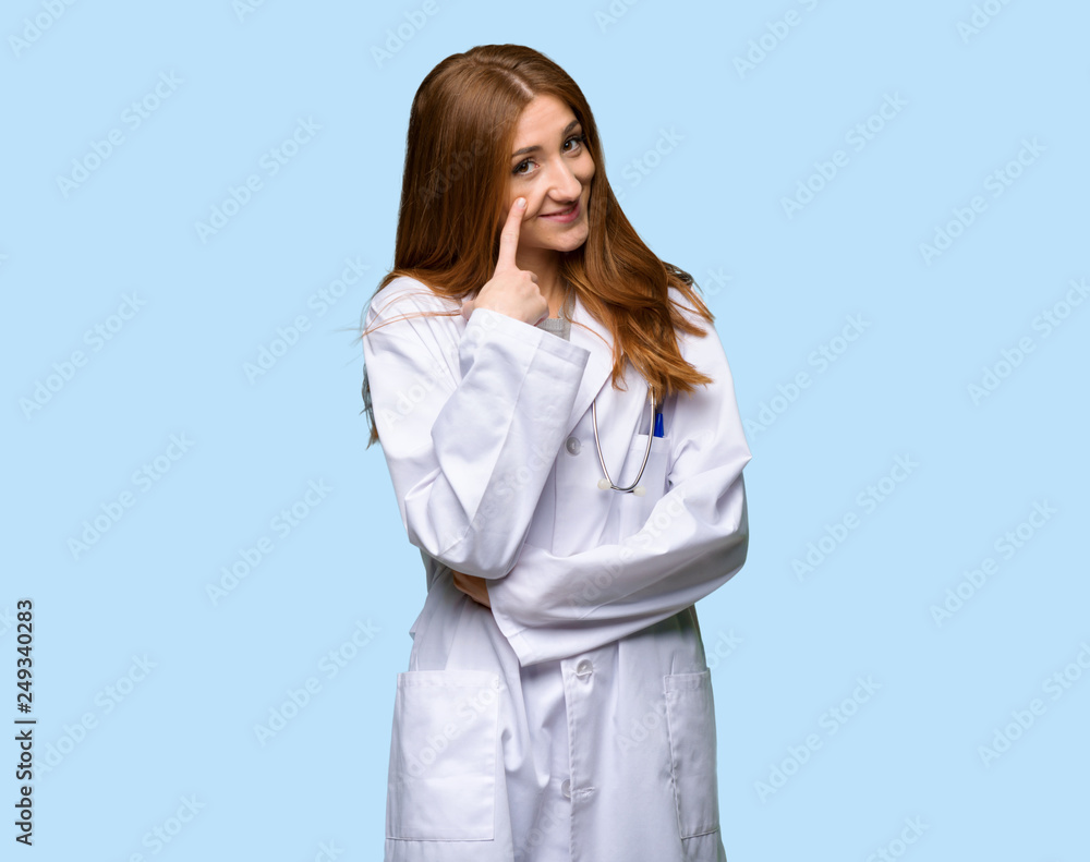 Redhead doctor woman looking to the front on isolated blue background Redhead doctor woman looking to the front on isolated blue background