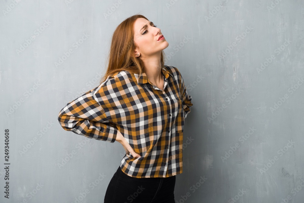 Young redhead girl over grunge wall suffering from backache for having made an effort Young redhead girl over grunge wall suffering from backache for having made an effort