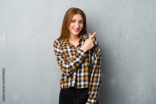 Young redhead girl over grunge wall pointing to the side to present a product