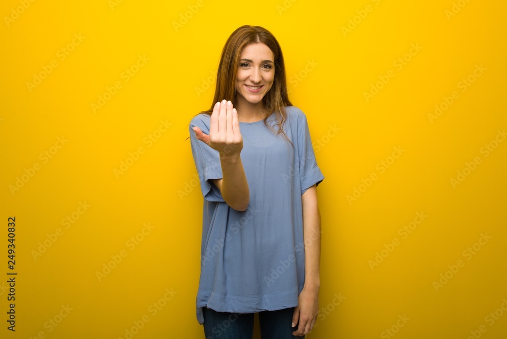 Young redhead girl over yellow wall background inviting to come with hand. Happy that you came Young redhead girl over yellow wall background inviting to come with hand. Happy that you came