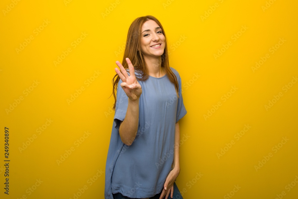 Young redhead girl over yellow wall background happy and counting three with fingers Young redhead girl over yellow wall background happy and counting three with fingers