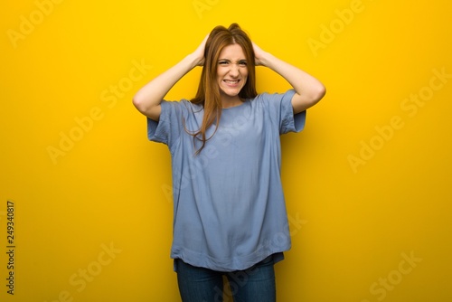 Young redhead girl over yellow wall background takes hands on head because has migraine © luismolinero