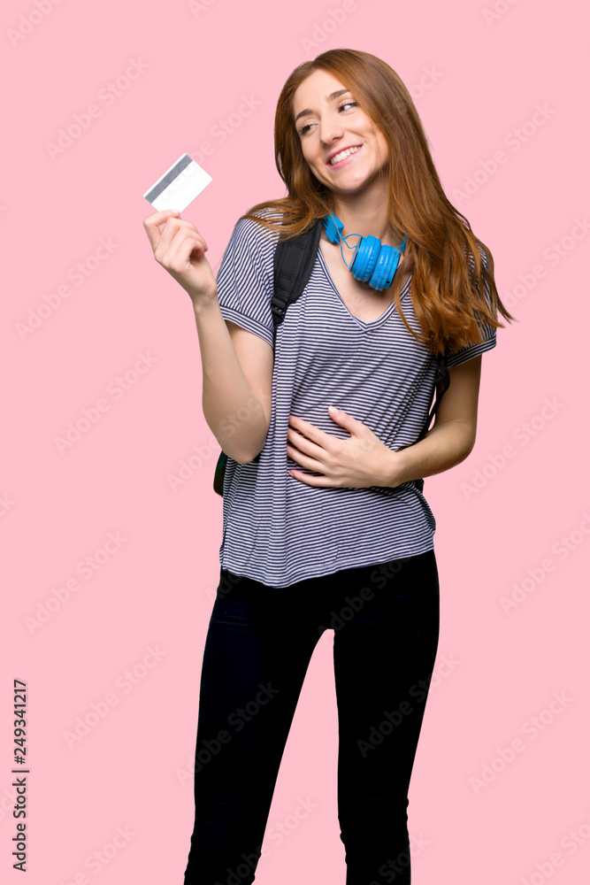Redhead student woman holding a credit card and thinking on isolated pink background Redhead student woman holding a credit card and thinking on isolated pink background