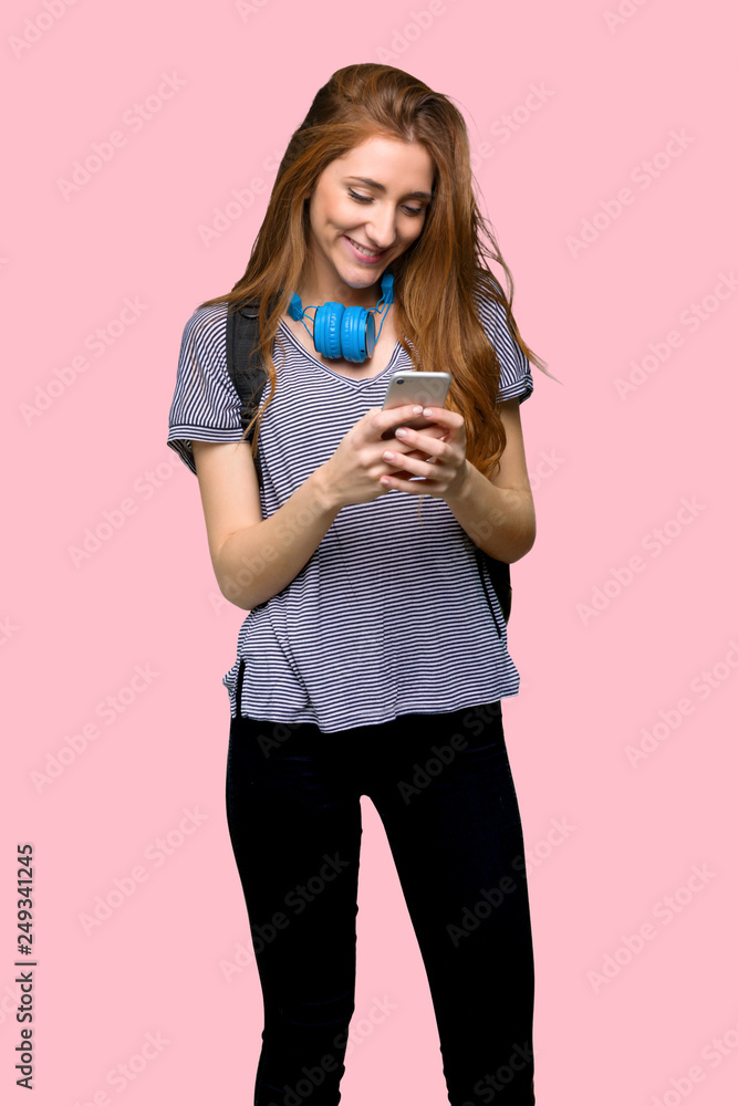 Redhead student woman sending a message with the mobile on isolated pink background Redhead student woman sending a message with the mobile on isolated pink background